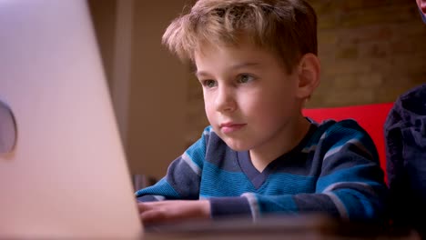 Close-up-profile-shoot-of-small-boy-playing-games-on-laptop-and-his-mother-observing-his-activity-sitting-nearby.