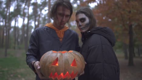 Zwei-Kaukasier-in-Halloween-Kostümen-mit-entsetzlichem-Make-up,-die-im-Herbstpark-in-die-Kamera-schauen