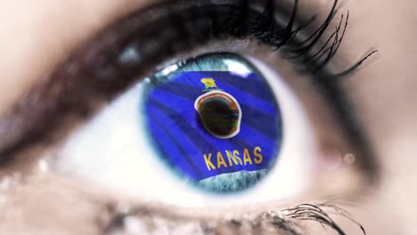 Woman-blue-eye-in-close-up-with-the-flag-of-Kansas-state-in-iris,-united-states-of-america-with-wind-motion.-video-concept