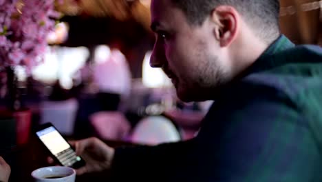 Young-man-sitting-at-a-bar-and-sending-message-on-the-mobile-phone