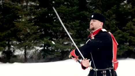 Ein-junger-Mann-in-Kosakenkleidung-schwingt-ein-Schwert-in-einer-Winterlandschaft-im-Schnee.