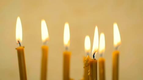 SLOW-MOTION:-close-up-of-a-lot-of-beautiful-wax-candles-burning.-Yellow-background.