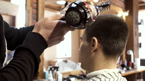 Hairdresser-dries-guy's-hair-with-hairdryer-in-barbershop