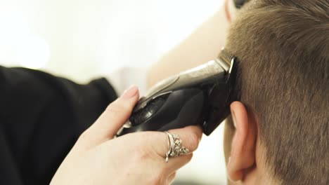 Corte-de-cabello-con-máquina-de-afeitar-eléctrica-en-barbería-de-cerca.-Peluquería-de-mujer-trabajando-con-el-cliente-y-haciendo-el-corte-de-pelo-masculino-con-máquina-de-afeitar-eléctrica