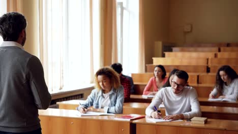 Männliche-Lehrer-erklärt-neuen-Informationen-zu-multi-ethnischen-Gruppe-von-Studenten,-die-in-Notizbüchern-Notizen-schreiben.-Beruf,-Bildung-und-Jugend-Konzept.