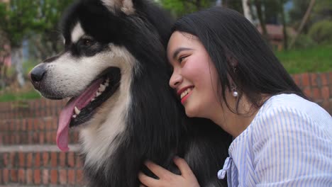 Cerca-de-joven-con-su-perro-malamute-de-Alaska-y-un-beso-al-aire-libre,-4k