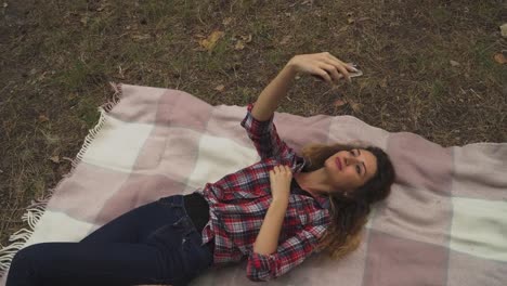 Mujer-joven-está-haciendo-selfie-tendido-sobre-la-manta-en-el-bosque