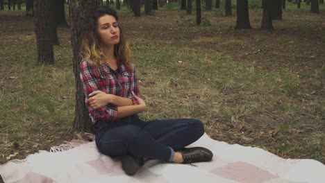 Redhead-woman-is-sitting-in-the-forest-near-the-tree