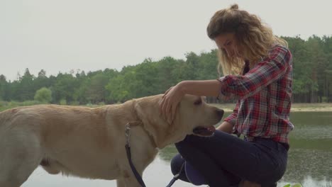 Lockige-Dame-ist-ihr-Hund-in-der-Nähe-des-Flusses-streicheln