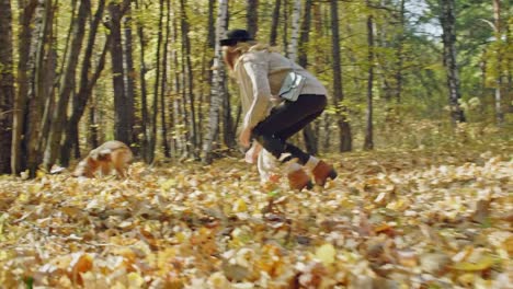 Muchacha-que-ríe-atrapar-su-perro-en-el-bosque-del-otoño