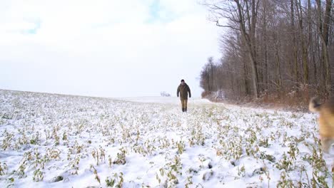 A-mature-man-in-his-fifties-walking-his-dog-on-a-beautiful-snowy-winter-morning.