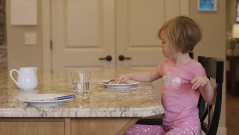 A-little-girl-eating-powdered-sugar-off-of-her-plate-with-her-fingers,-with-her-dog-begging-nearby