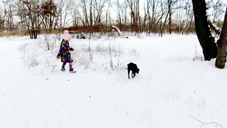 Kleines-Mädchen-spielt-mit-ihren-schwarzen-Labrador-auf-Schnee