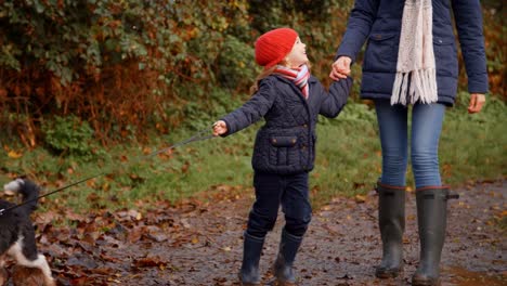 Mutter-und-Tochter-nehmen-Hund-für-Spaziergang-in-Herbst-Landschaft