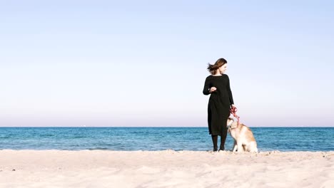 Young-female-standing-with-siberian-husky-dog-with-beach-background