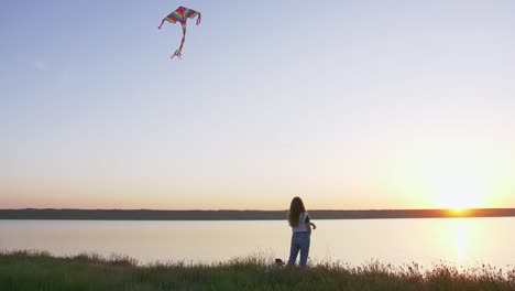 Junge-Frau-glücklich-und-Het-Hündchen-mit-Drachen-auf-der-Waldwiese-bei-Sonnenuntergang,-niedrigen-Winkel-Ansicht