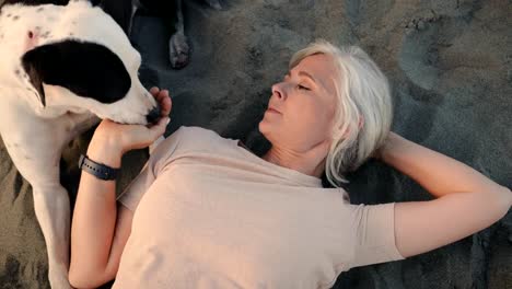 Mujer-madura-feliz-tumbado-en-la-playa-con-perro-de-animal-doméstico