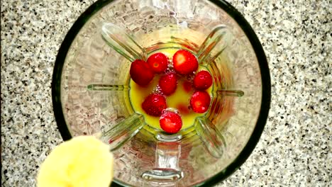 Stücke-von-Bananen-fallen-auf-Erdbeere-in-Orangensaft.-Slow-Motion.	Dreharbeiten-in-der-Küche.-Ansicht-von-oben.