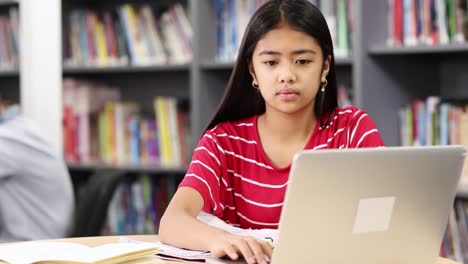 Female-High-School-Student-Working-At-Laptop-In-Library