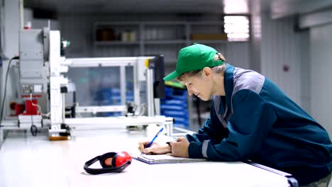 elderly-woman,-employee,-worker-at-an-enterprise,-factory,-fills-up-a-service-journal,-record-book,-working-industrial-background