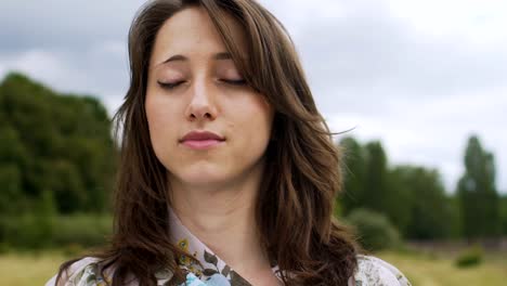 Young-female-stands-with-eyes-closed-outdoors,-feeling-herself-and-world-around