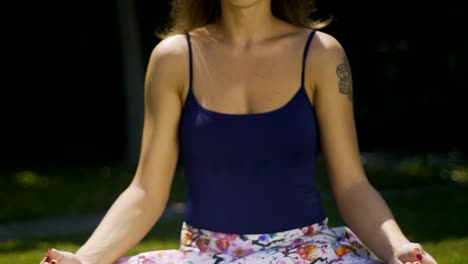 Female-yogi-meditates-outdoors-sits-in-lotus-position-pan,-face-close-up-park