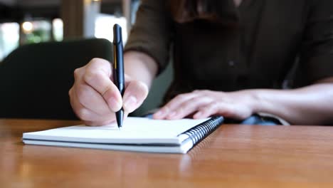 die-Hand-einer-Frau-schreiben-auf-leere-Notebooks-auf-Holztisch