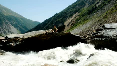 Man-sits-in-a-lotus-position-and-meditates-in-mountains.-River-flows-fast