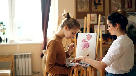 Junge-Frauen-Kunstlehrer-und-Schüler-haben-Unterricht-in-Malschule,-Mädchen-ist-Farben-auf-der-Palette-mischen,-während-Meister-im-Gespräch-mit-Lernenden-berät.