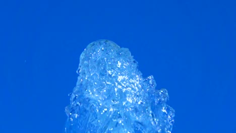 A-splash-of-clear-ice-water.-Closeup-of-light-splashing-water-in-sunny-fountain-in-park-in-summer-on-blue-sky-background.--Water-flow-of-fountain-fly-up-in-air-with-many-splashes.-Slow-motion.