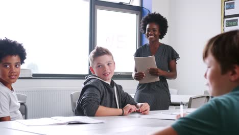 Weibliche-High-School-Tutor-Lehre-Gruppe-von-Studenten-um-Tisch-im-Klassenzimmer