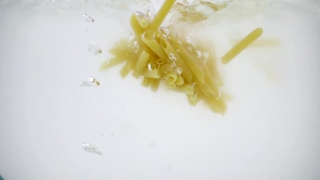 Stuck-together-cheap-tasteless-pasta-thrown-into-boiling-water,-shot-in-slow-motion-on-white-background,