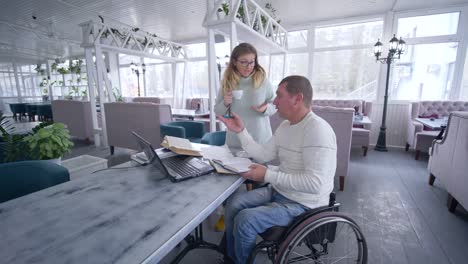 freelance-lifestyle-of-invalid,-Creative-disabled-man-on-wheelchair-with-female-with-cup-coffee-discussing-startup-business-during-working-on-laptop-for-planning-and-managing-business