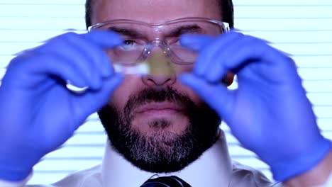 Biologist-examines-sample.-Science,-biology,-ecology.-Professional-scientist-wearing-protective-mask-working-with-herb-samples-in-his-laboratory.-Male-scientist-looking-at-plant-leaf-in-glass-slide.