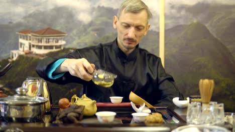 Tee-Zeremonie.-Master-Man-gießt-grüner-Tee-aus-einem-Glas-Teekanne-in-eine-weiße-Tasse