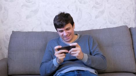 Man-is-playing-game-on-his-mobile-phone-sitting-on-the-sofa.