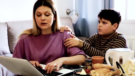 woman-working--and--sad--boy-standing-near-table-at-home