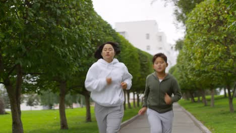 Sportliche-asiatische-Mutter-und-Sohn-Joggen-entlang-Green-Alley-mit-Bäumen