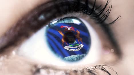 Woman-blue-eye-in-close-up-with-the-flag-of-Michigan-state-in-iris,-united-states-of-america-with-wind-motion.-video-concept