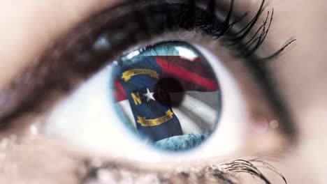 Woman-blue-eye-in-close-up-with-the-flag-of-North-Carolina-state-in-iris,-united-states-of-america-with-wind-motion.-video-concept