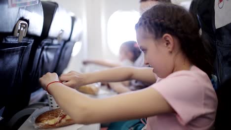 Young-woman-sits-in-chair-near-illuminator-of-airplane-and-eats-meal-for-passenger