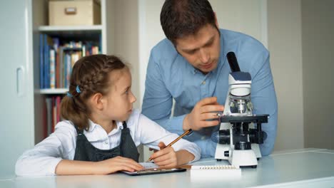 Kleines-Mädchen-mit-Lehrer-im-naturwissenschaftlichen-Unterricht-mit-Mikroskop-auf-dem-Tisch.