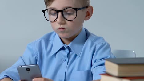 Adorable-school-boy-in-glasses-playing-smartphone-game-in-classroom-during-break