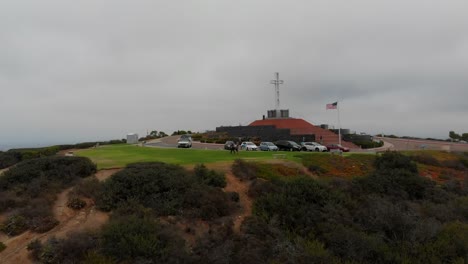 Aerial-Shot-Revealing-and-Flying-Over-the-Mt.-Soledad-Cross-Monument-in-San-Diego,-California-with-Trees,-Hills,-Cars,-and-Homes-in-View.