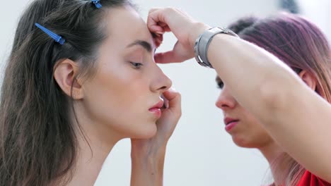 Close-up-professional-make-up-artist-working-with-eyes-makeup-on-face-of-young-female-model