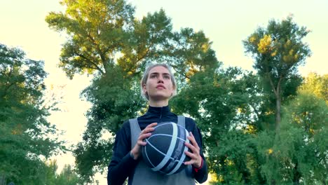 Confident-blonde-female-basketball-player-holding-ball-and-walking-in-park,-low-angle,-wearing-sportswear