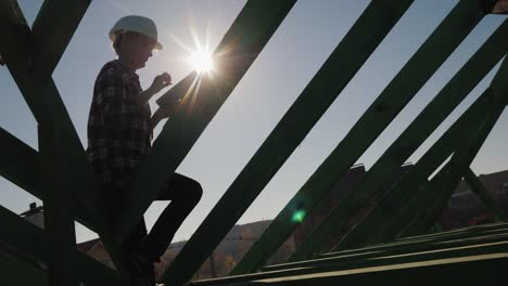 Silhouette-of-an-engineer,-works-among-the-rafters-of-the-roof,-uses-a-tablet.-Technical-control-in-construction