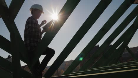 Silueta-de-un-ingeniero,-trabajos-entre-las-vigas-del-techo,-utiliza-una-tableta.-Control-técnico-en-construcción