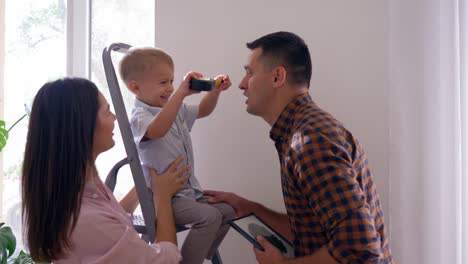 familia-joven-con-hijo-pequeño-haciendo-reparaciones-y-colgante-estante-de-pared-en-casa