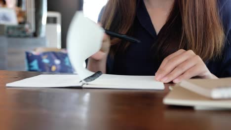 Closeup-imagen-de-una-mujer-abriendo-un-cuaderno-en-blanco-para-escribir-en-la-mesa-de-madera